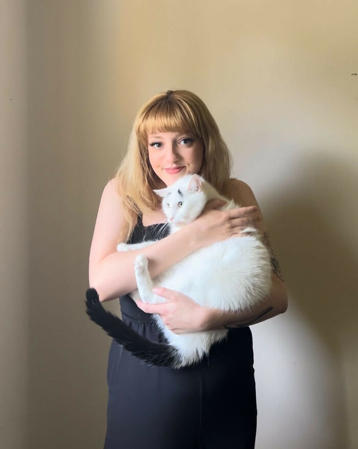 Woman holding a white cat with a black tail and eyebrows 