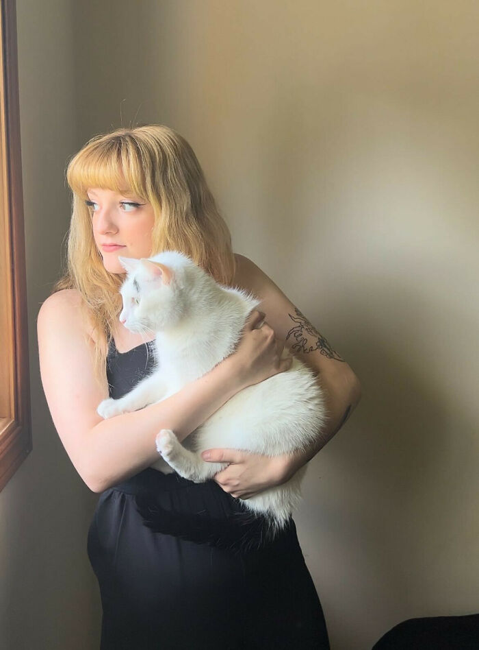 Woman holding a white cat with a black tail and eyebrows 